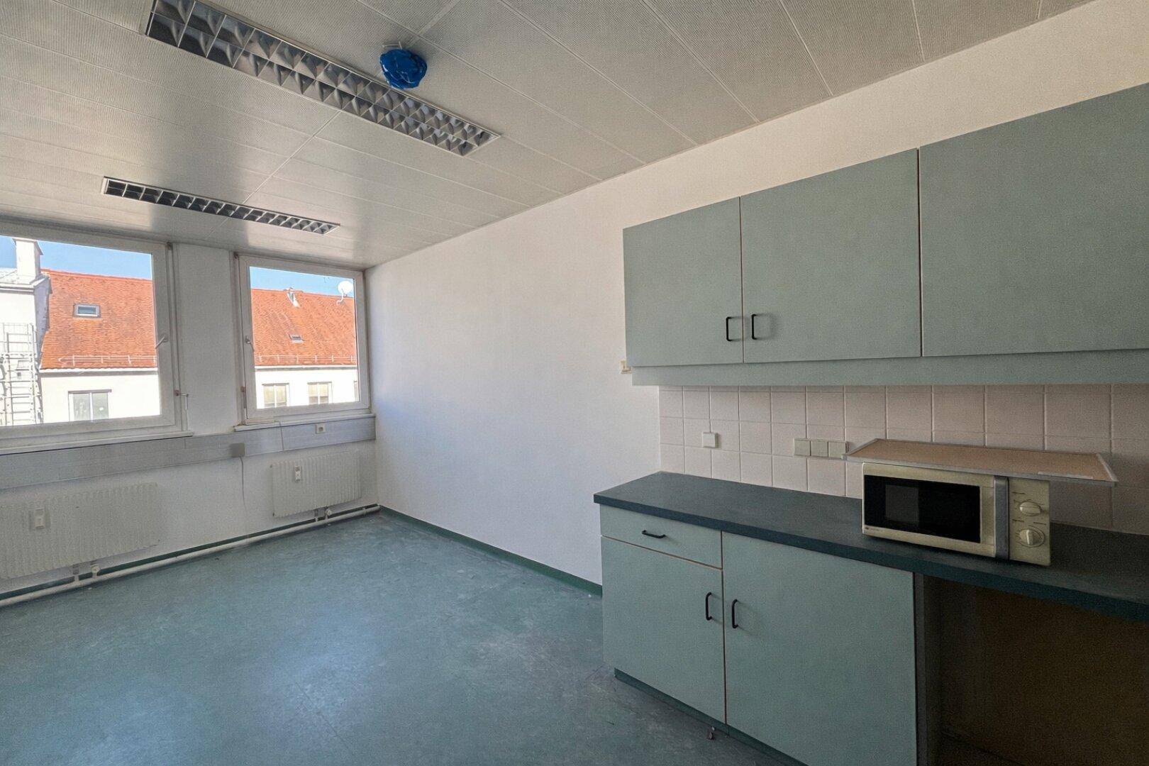 Kleine Teeküche mit hellblauen Schränken, Mikrowelle und dunklem Bodenbelag, ideal für Pausen.