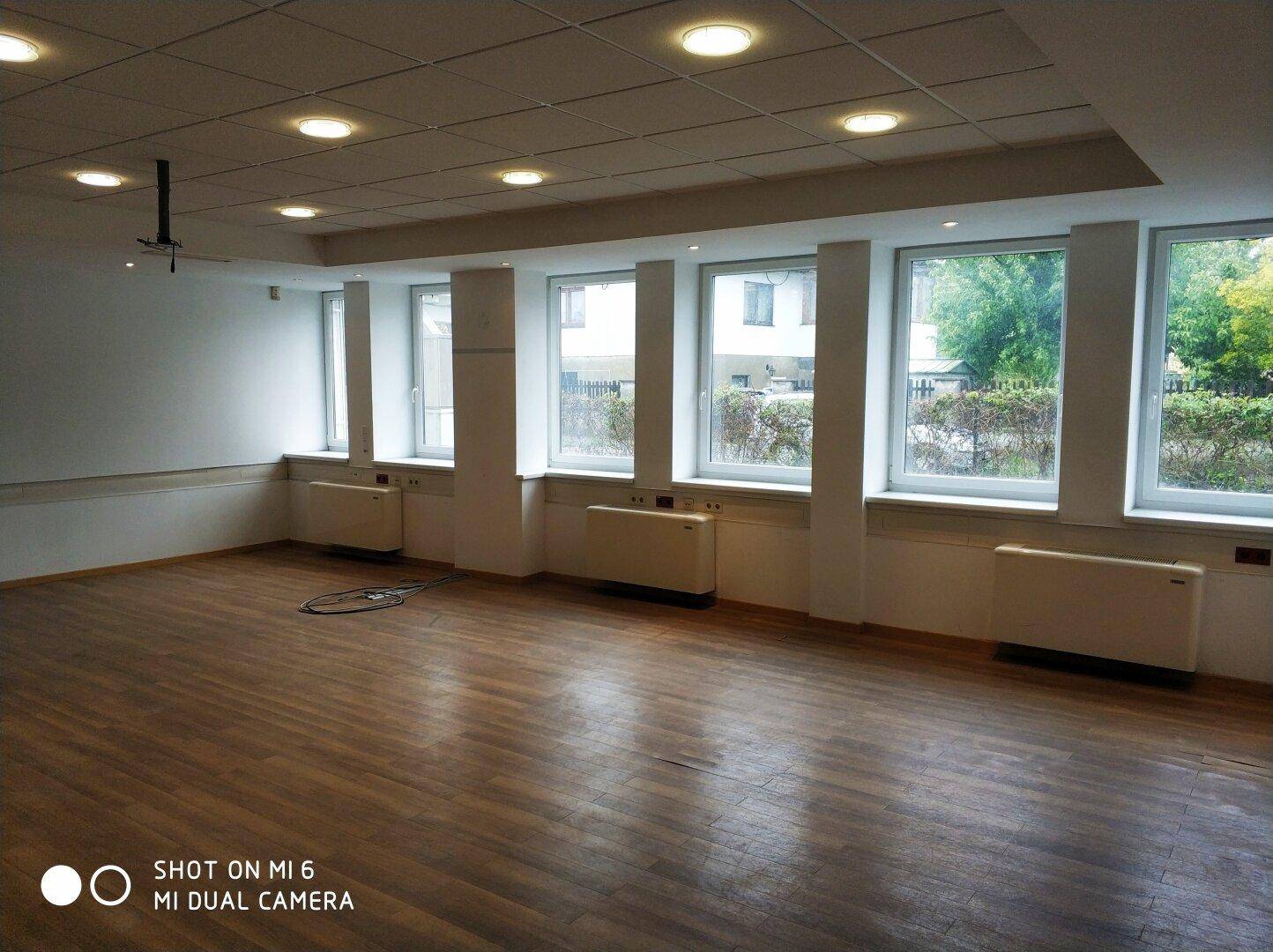 Geräumiger Konferenzraum mit Laminatboden, vielen Fenstern und abgehängter Decke mit Einbauleuchten.
