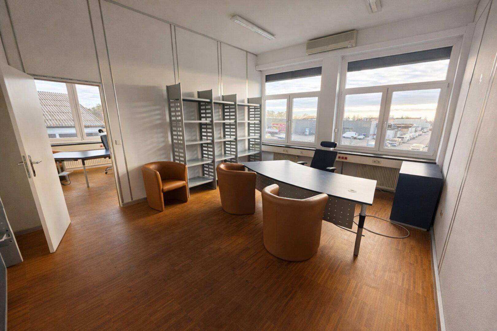 Helles Büro mit Laminatboden, großen Fenstern, braunen Sesseln und Blick auf ein Gewerbegebiet.