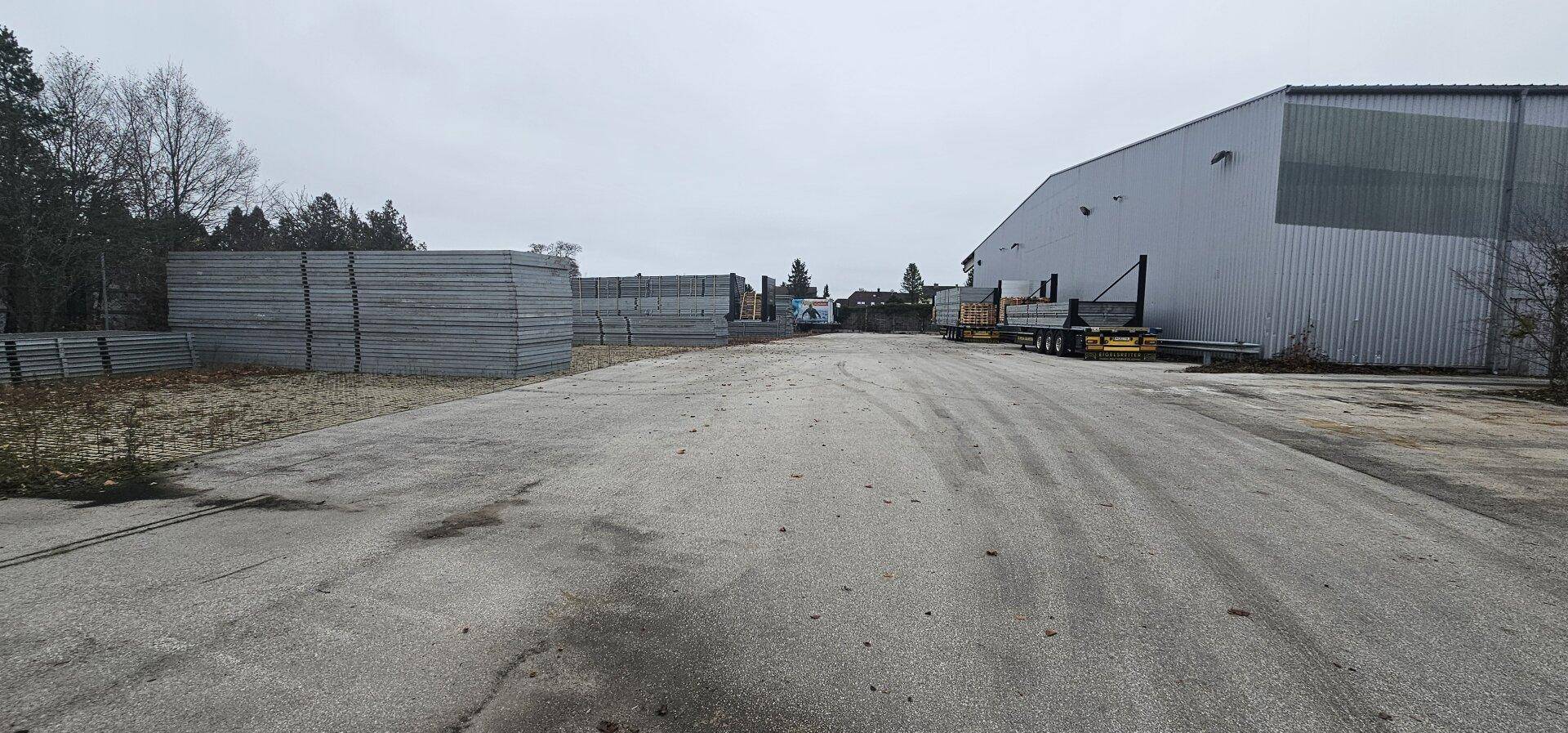 Weitläufiger Außenbereich mit einer großen Lagerhalle und hohen Stapeln von Baumaterialien unter bewölktem Himmel.