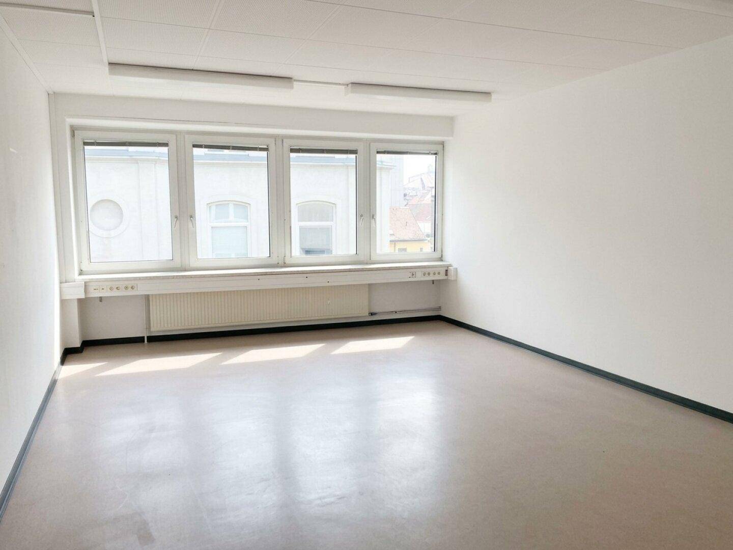 Heller, leerer Büroraum mit großen Fenstern, die viel Tageslicht hereinlassen und einem hellen Bodenbelag.