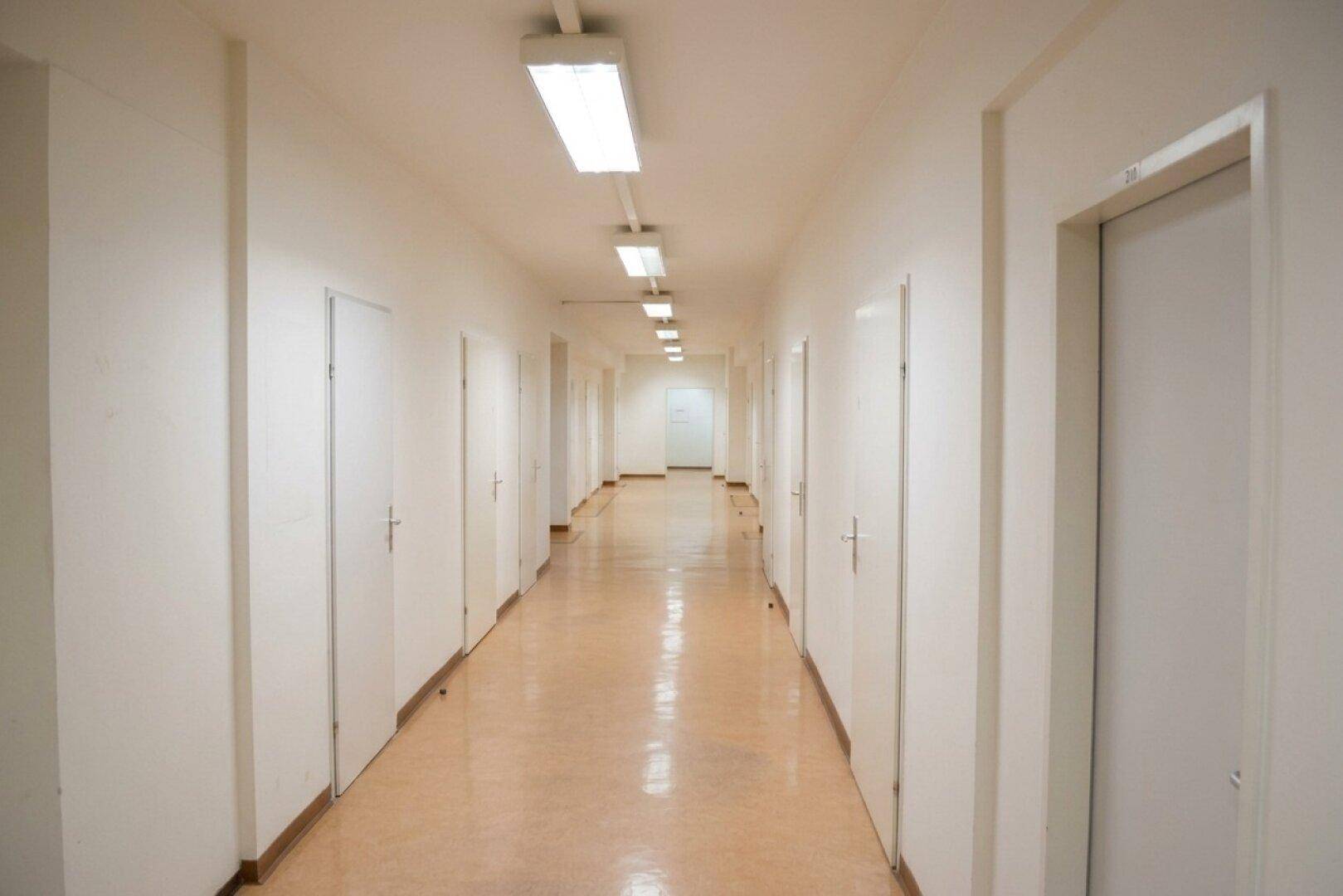 Langer, gut beleuchteter Flur mit zahlreichen Türen auf beiden Seiten und einem hellen Bodenbelag.