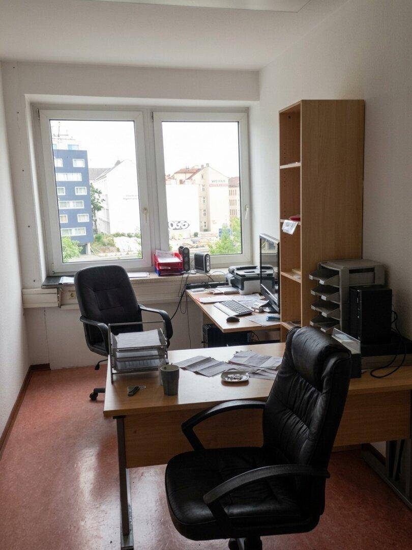 Funktionales Büro mit Schreibtisch, Bürostühlen und Blick auf umliegende Gebäude durch das Fenster.