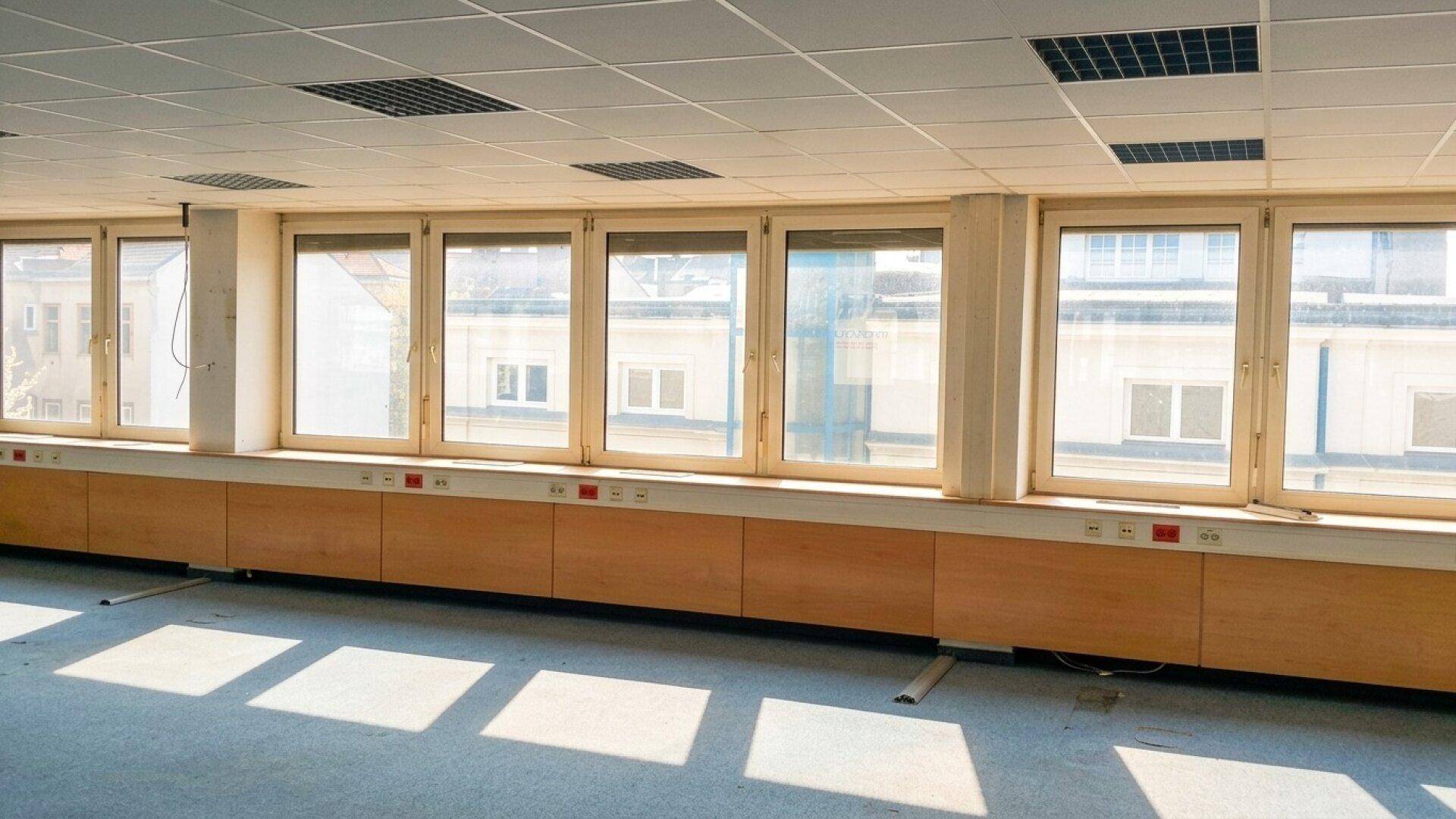 Großer Büroraum mit vielen Fenstern, die viel Licht hereinlassen, und einer abgehängten Decke.