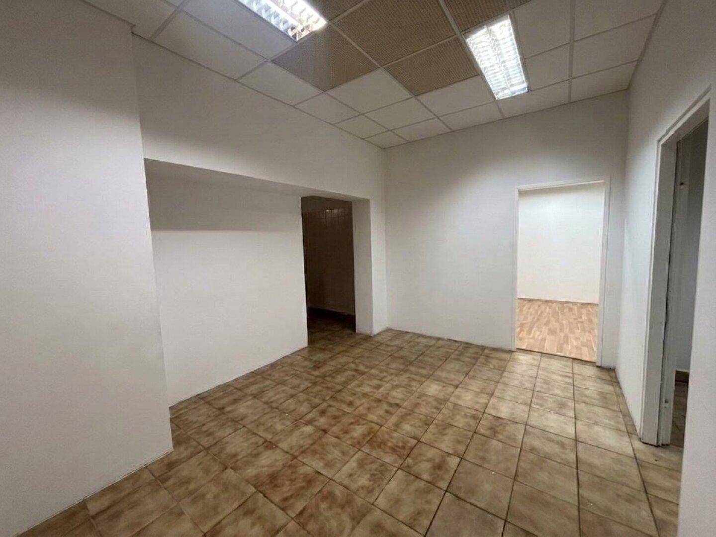 Leerer Büroraum mit Fliesenboden und abgehängter Decke, bereit zur individuellen Gestaltung.