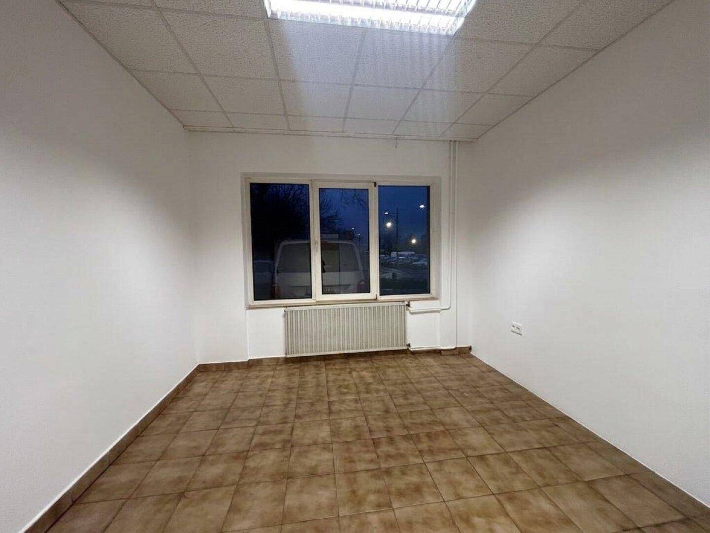 Heller Büroraum mit Fliesenboden, großem Fenster und Heizkörper unter der Fensterbank.