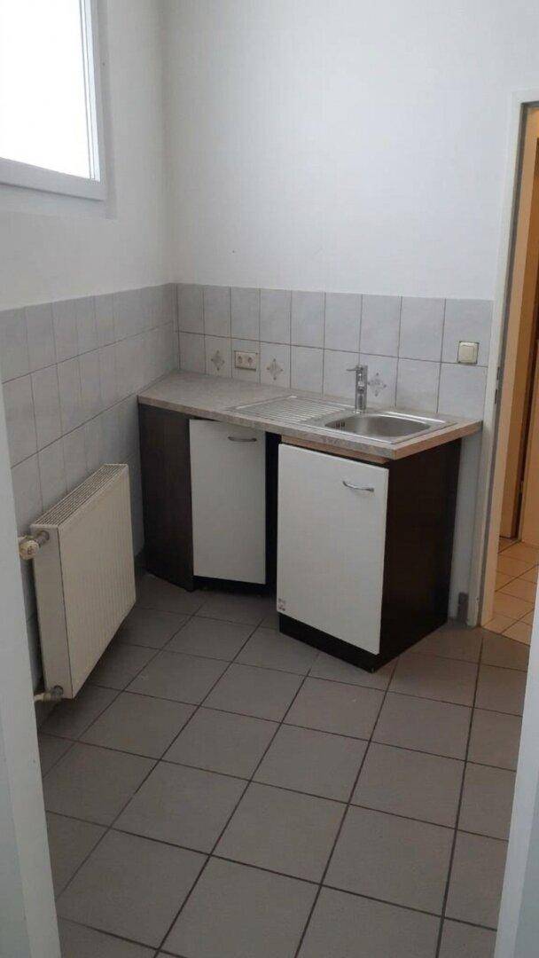 Kleine Küchenzeile mit Doppelspüle, Unterschränken und Fliesenboden in einem funktionalen Nebenraum.