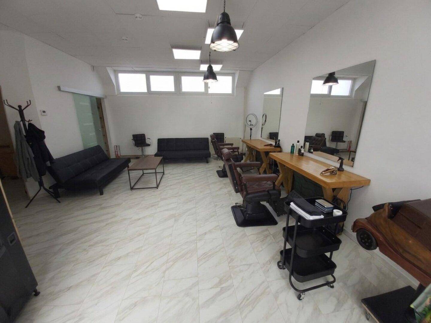 Moderner Friseursalon mit hellen Fliesen, dunklen Möbeln und großen Spiegeln, gut beleuchtet.