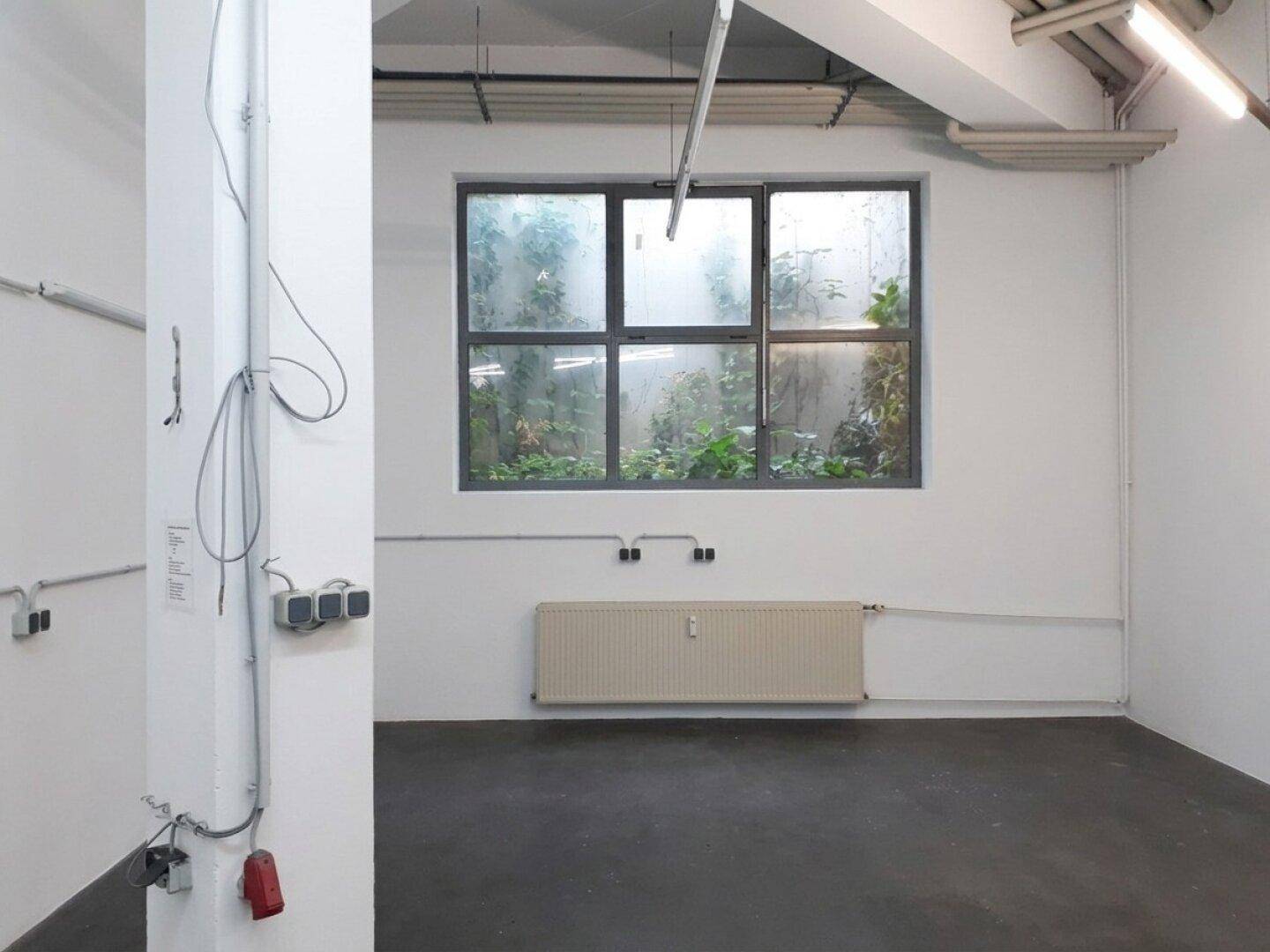 Nahaufnahme eines großen Fensters in einem Gewerberaum mit Heizkörper und sichtbaren Installationen.