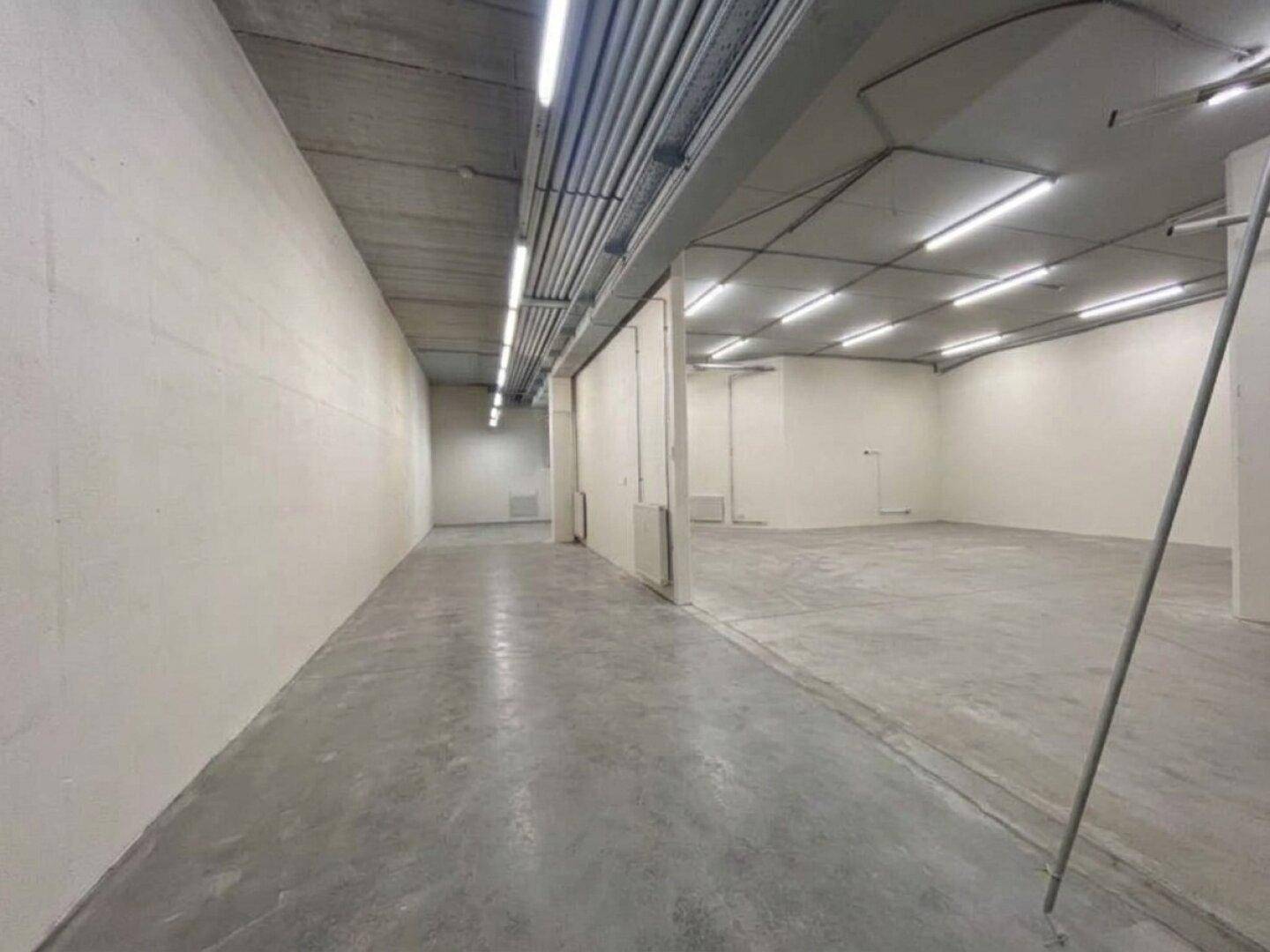 Langer Flur in einem Gewerbeobjekt mit Betonboden, weißen Wänden und sichtbaren Deckeninstallationen.