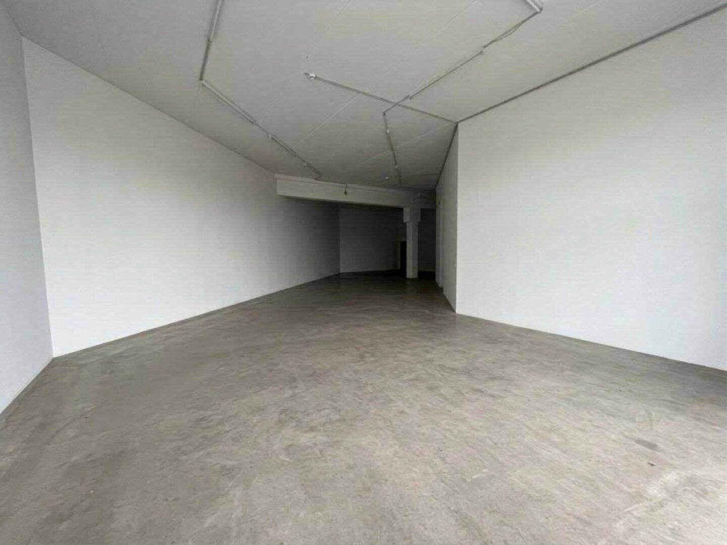 Helle, unmöblierte Gewerbefläche mit hohen Decken und einem strapazierfähigen Betonboden, bereit für den Ausbau.