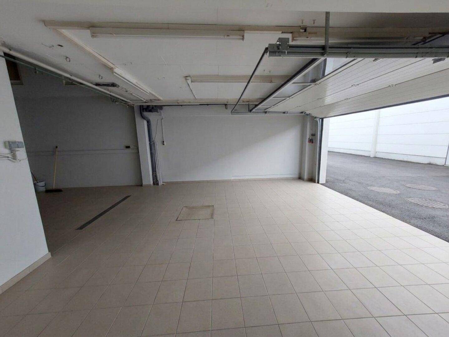 Geräumige Garage mit Fliesenboden und offenem Garagentor, das den Zugang zum Außenbereich ermöglicht.