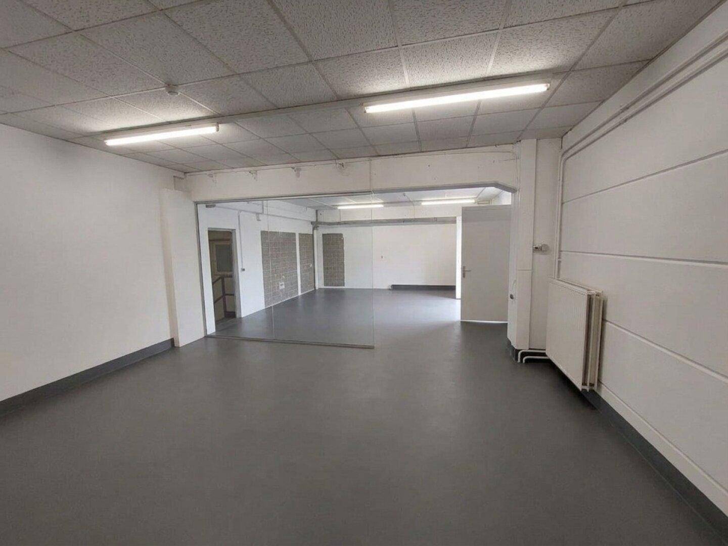 Großer, leerer Gewerberaum mit grauem Boden und Rasterdeckenplatten, ideal für verschiedene Nutzungen.