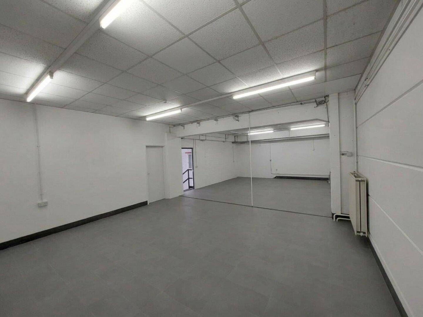Geräumiger Gewerberaum mit grauem Boden, Rasterdecke und einer großen Spiegelwand.