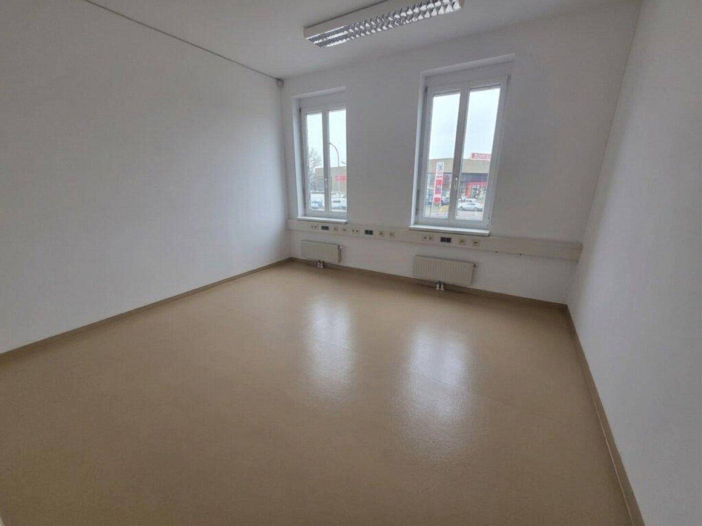 Sauberer und heller Büroraum mit zwei Fenstern, Heizkörpern und praktischem Bodenbelag.