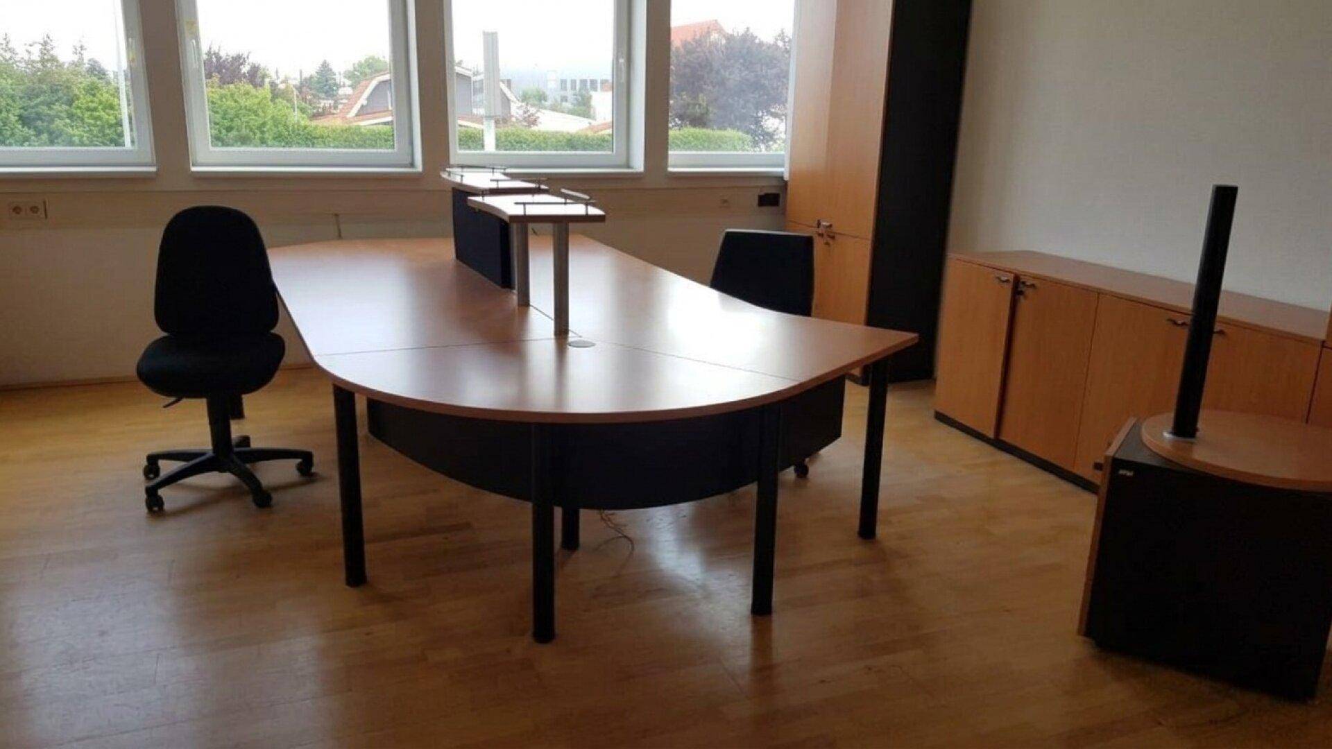 Geräumiger Büroraum mit großen Fenstern, Holzboden und funktionalen Büromöbeln.