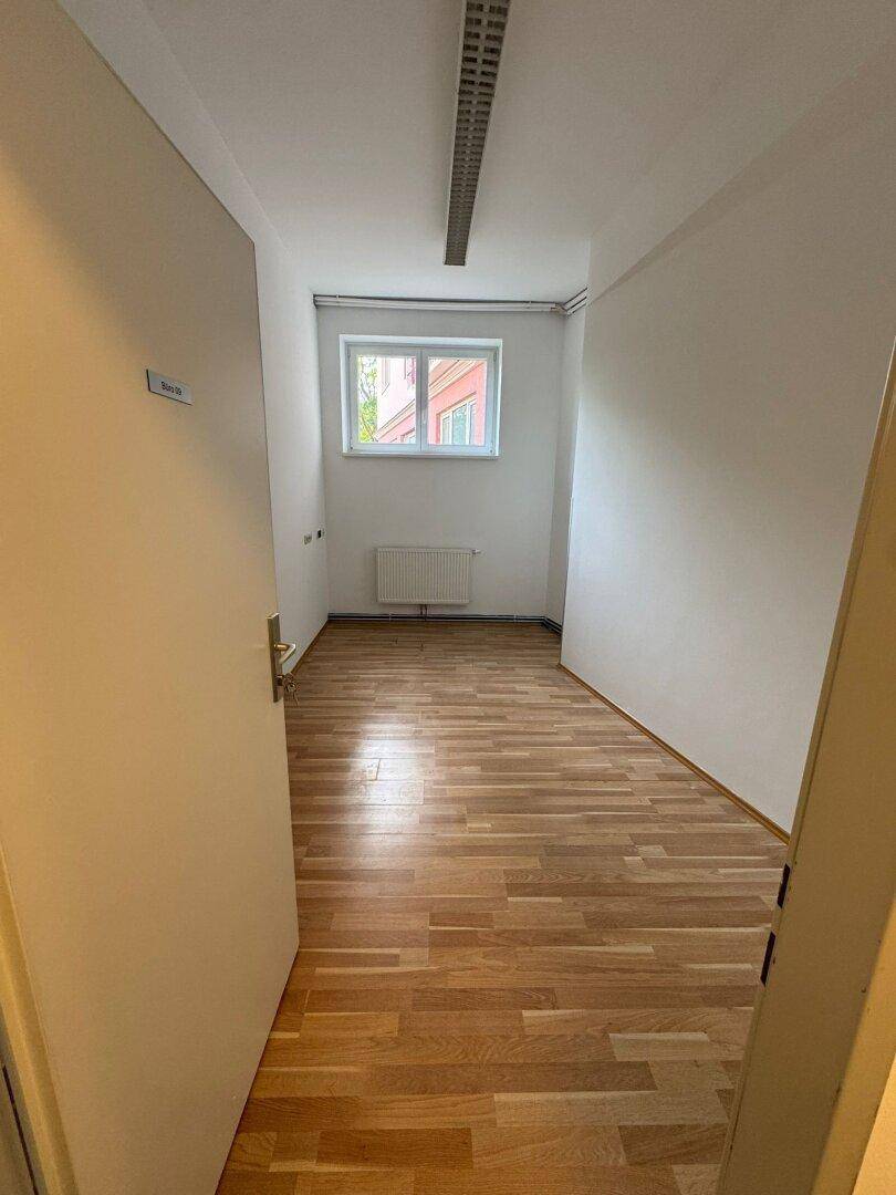 Heller, leerer Raum mit Holzparkettboden, einem Fenster und Heizkörper unter der Fensterbank.