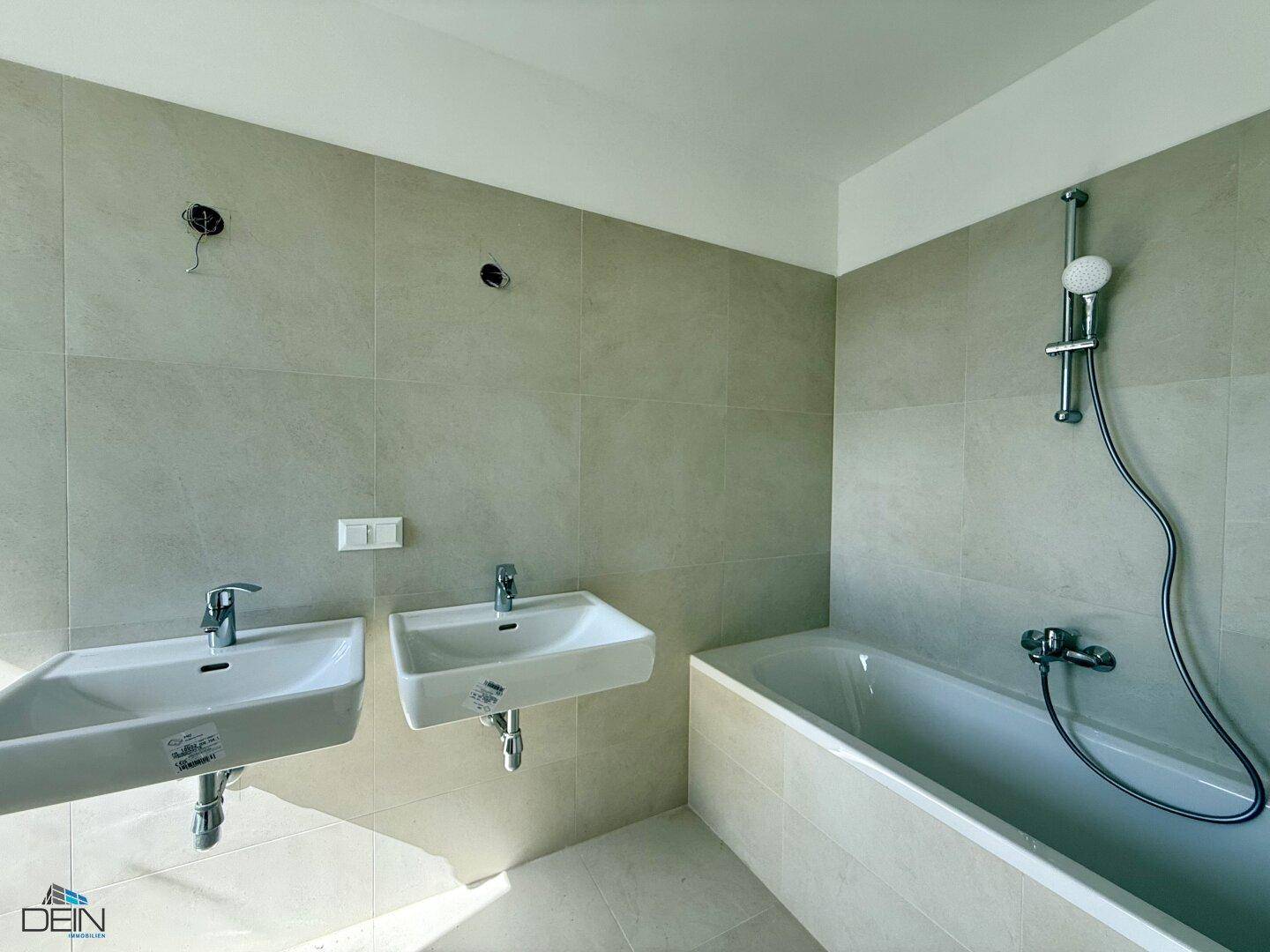 Badezimmer mit Badewanne, zwei Waschbecken und hellen Wandfliesen.
