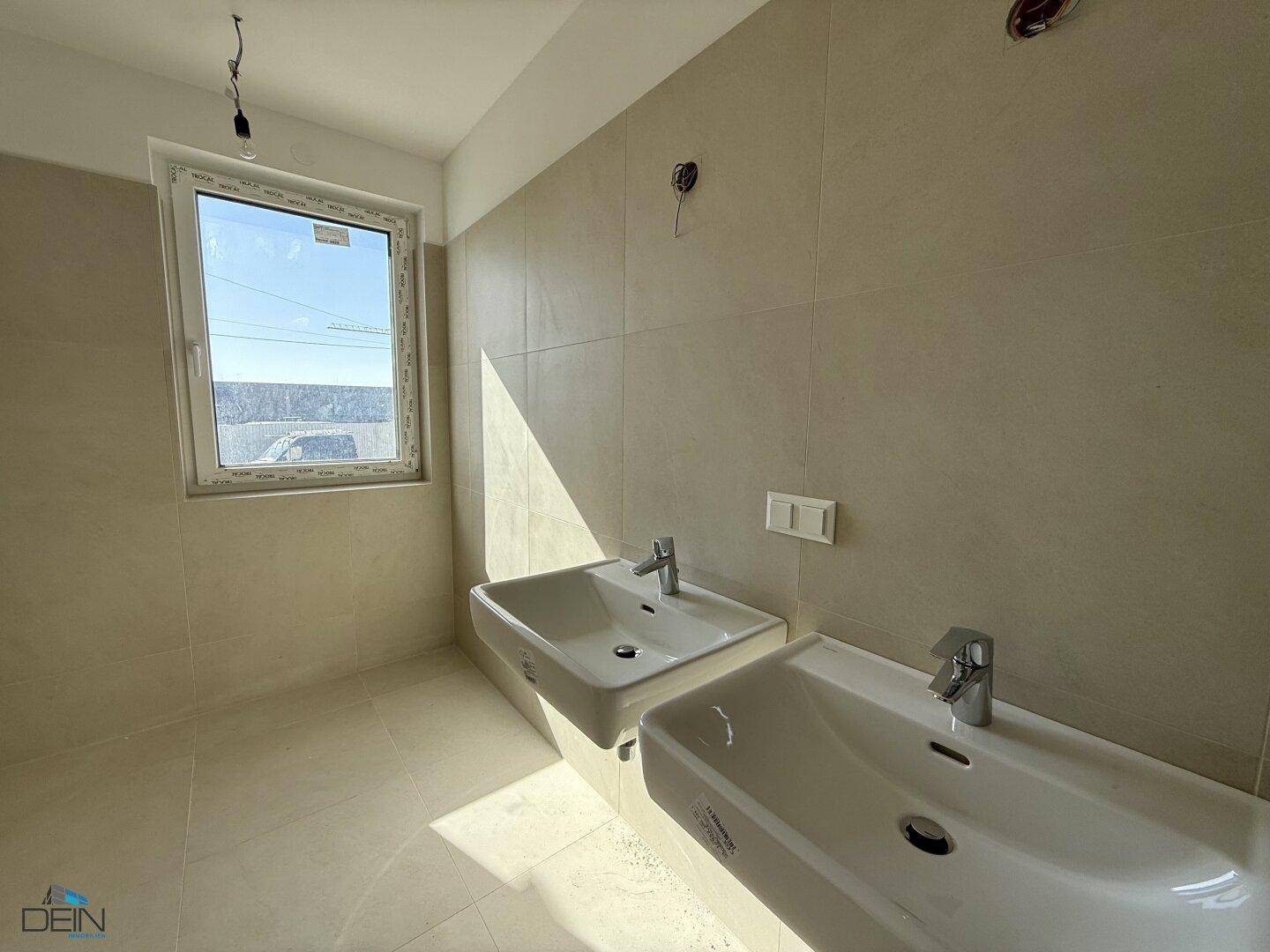 Helles Badezimmer mit zwei Waschbecken und großformatigen Fliesen.
