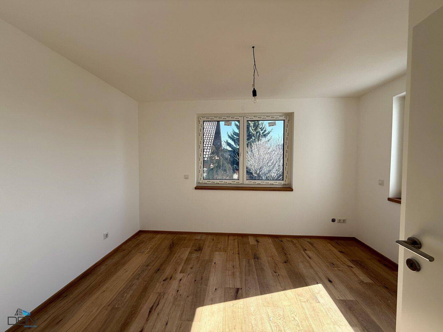 Geräumiges Schlafzimmer mit Holzboden und Blick ins Grüne durch das Fenster.
