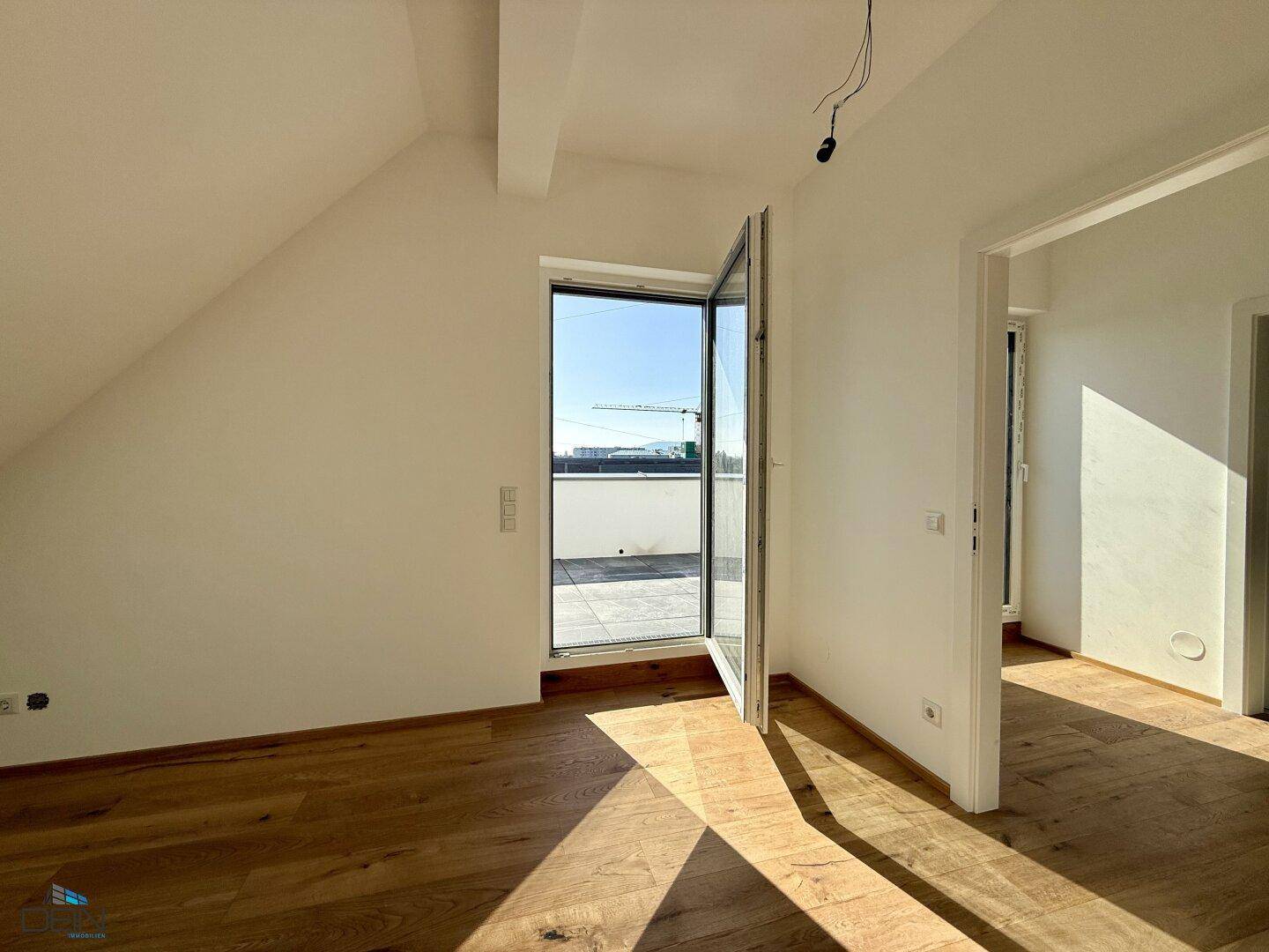 Helles Dachzimmer mit Zugang zu einer Dachterrasse und Holzboden.