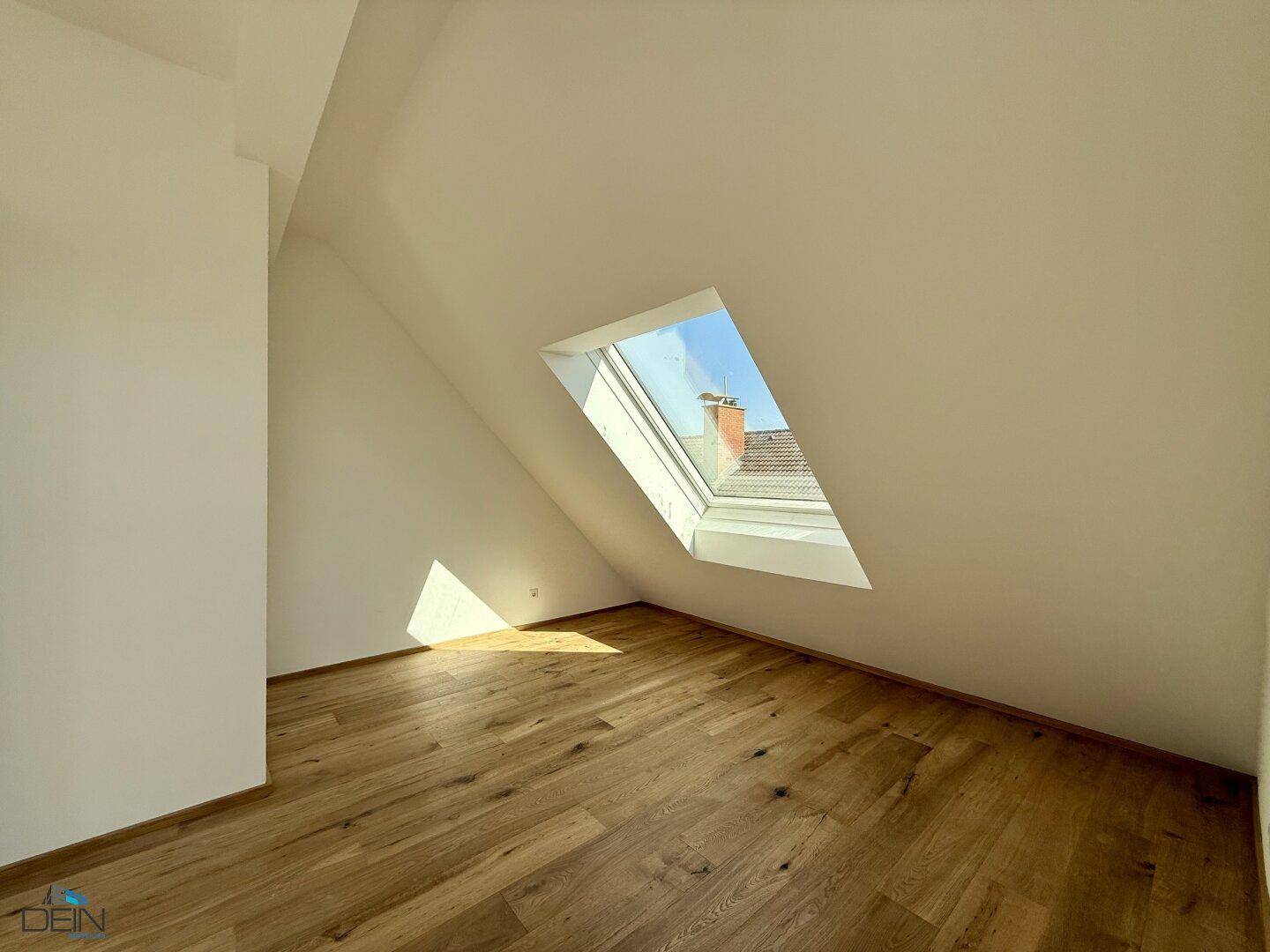 Dachzimmer mit Holzboden und einem Dachfenster, das viel Licht spendet.