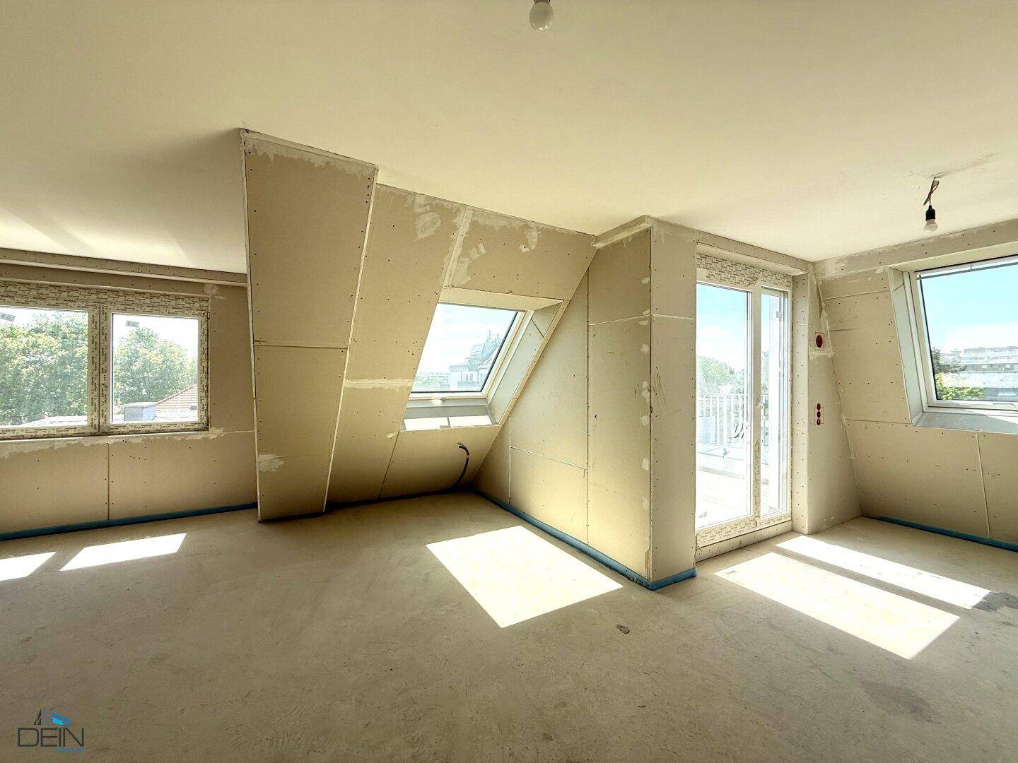 Unfertiger Innenraum mit Dachschrägen, Trockenbauwänden, Dachfenster und Zugang zu einem französischen Balkon.