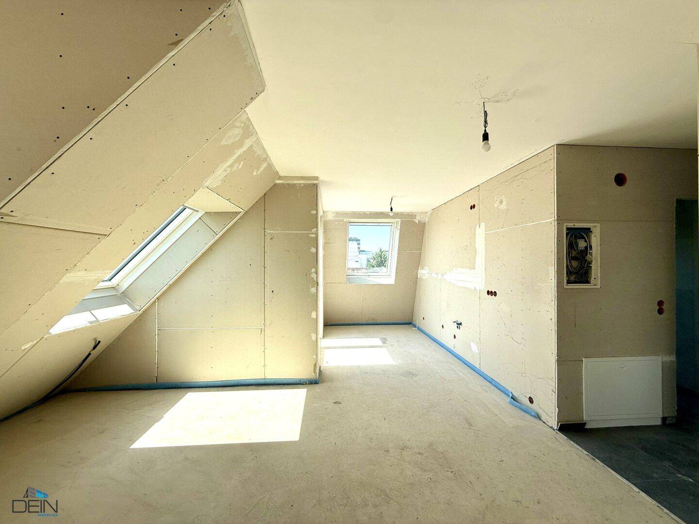 Rohbauzimmer mit Dachschrägen, Trockenbauwänden und einem weiteren Dachfenster, das viel Licht hereinlässt.