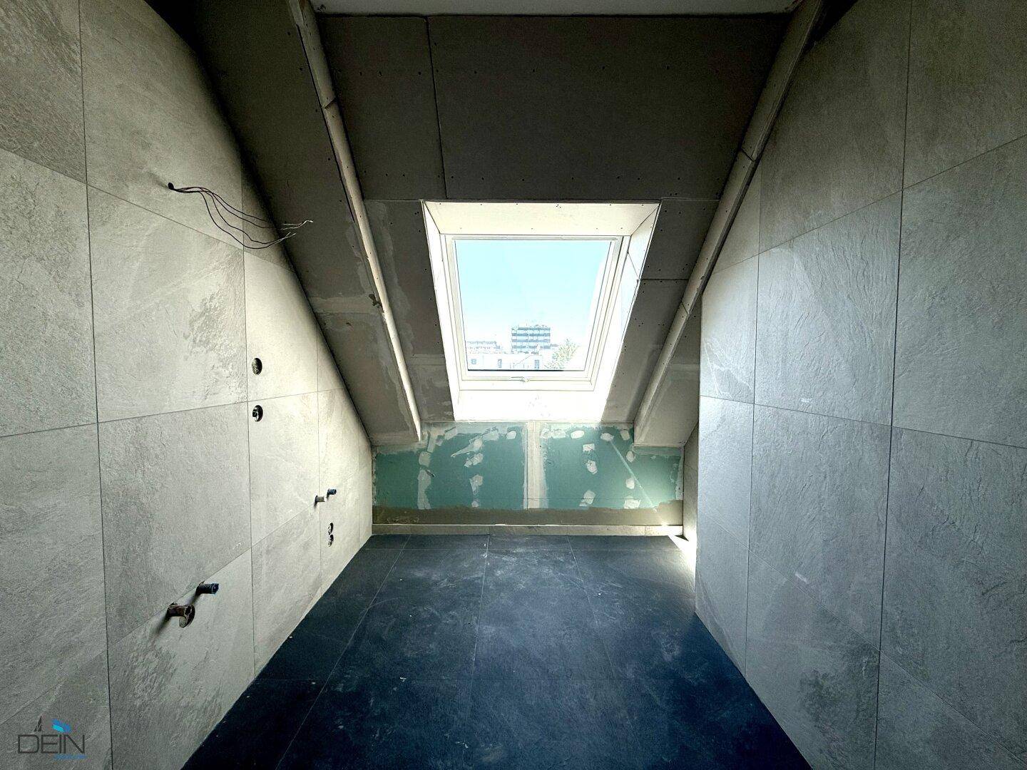 Rohbaubadezimmer mit gefliesten Wänden, Dachschräge und einem Dachfenster für natürliche Belüftung.
