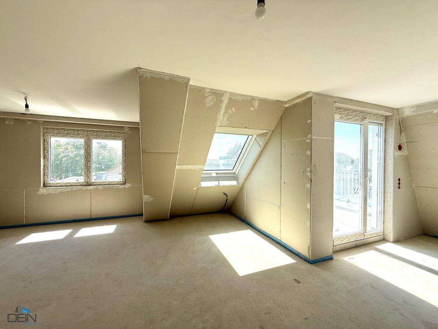 Heller Raum im Rohbau mit Dachschrägen, großem Dachfenster und Zugang zu einem französischen Balkon.