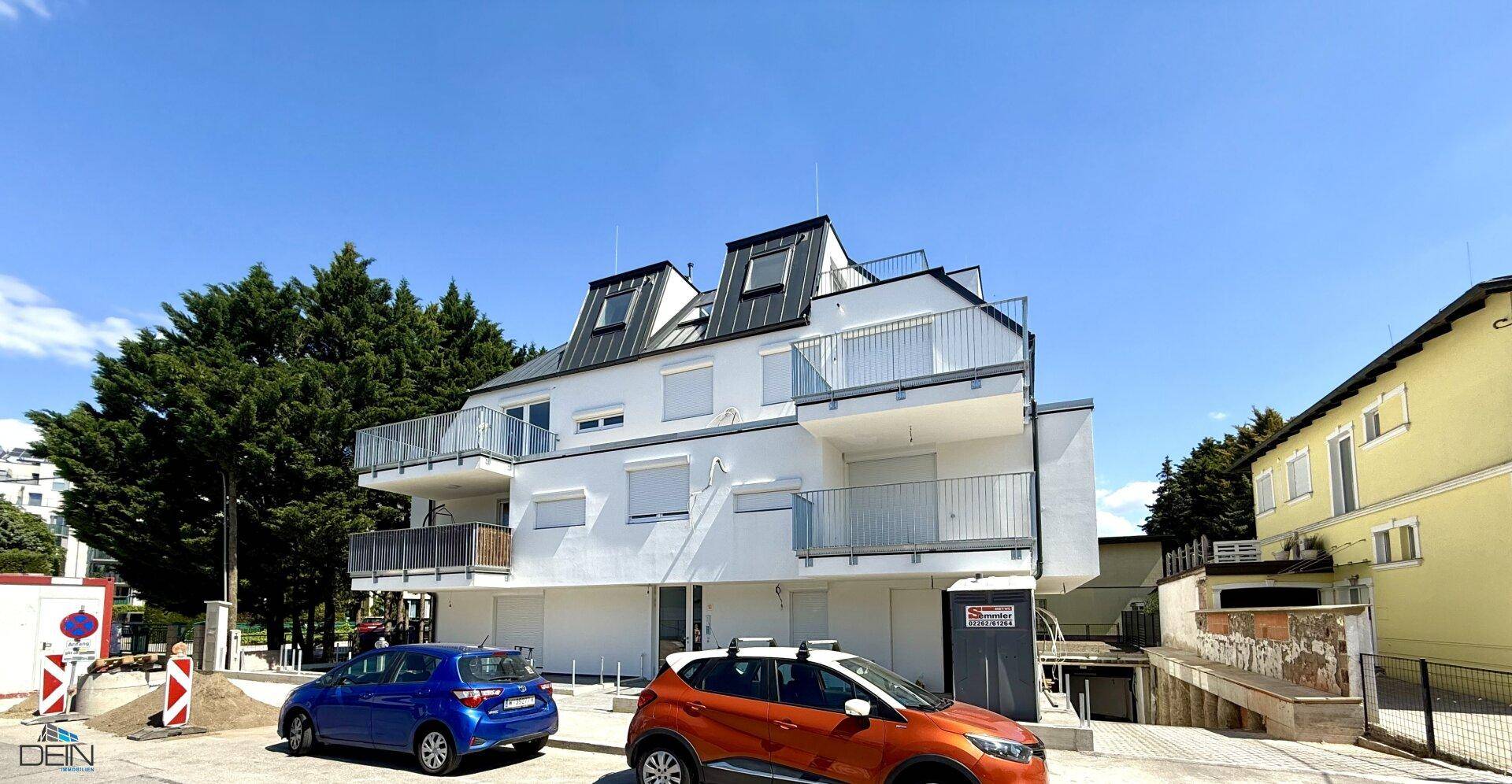 Ansicht des modernen Apartmentgebäudes von der Straße aus mit Balkonen und geparkten Autos.