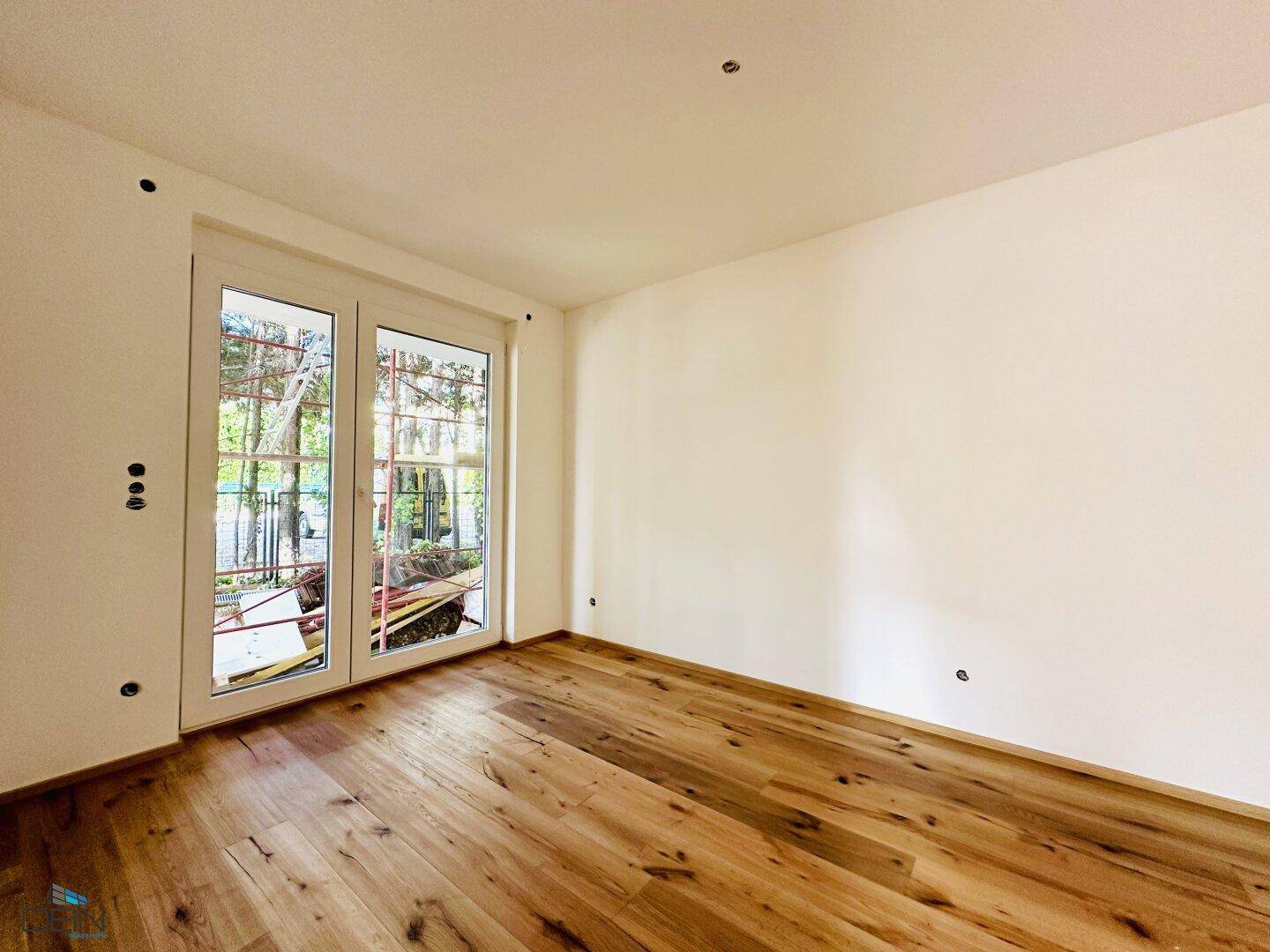 Lichtdurchfluteter Raum mit elegantem Holzplankenboden und breiten Glastüren, die den Zugang nach draußen ermöglichen.
