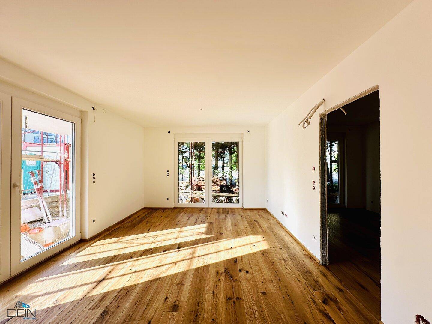 Helles Wohnzimmer mit hochwertigem Holzplankenboden und großen Glastüren, die viel Licht hereinlassen.