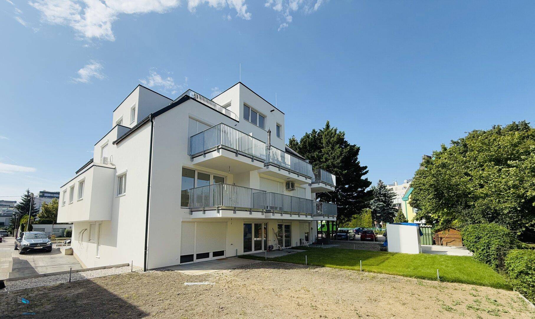 Modernes Mehrfamilienhaus mit weißer Fassade, mehreren Balkonen und umliegender Grünfläche.