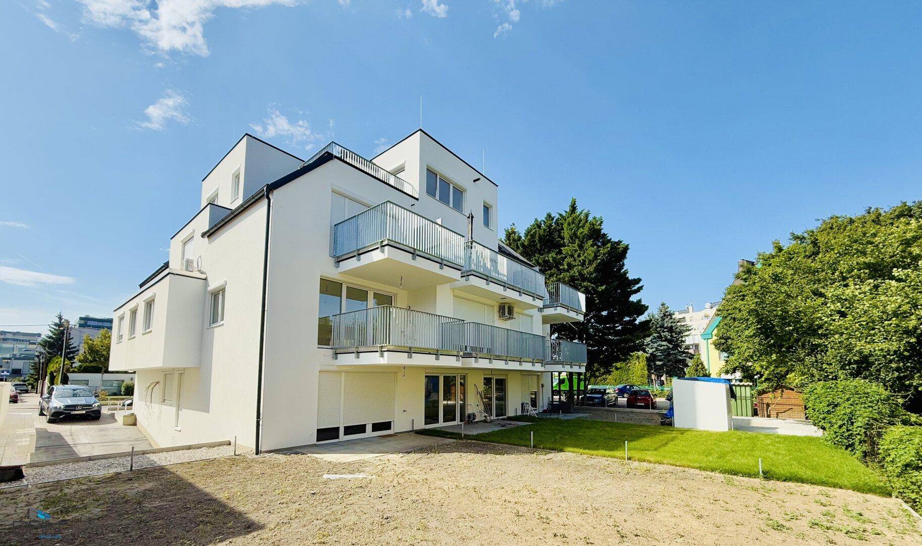 Modernes weißes Mehrfamilienhaus mit mehreren Balkonen und großen Fenstern unter blauem Himmel.