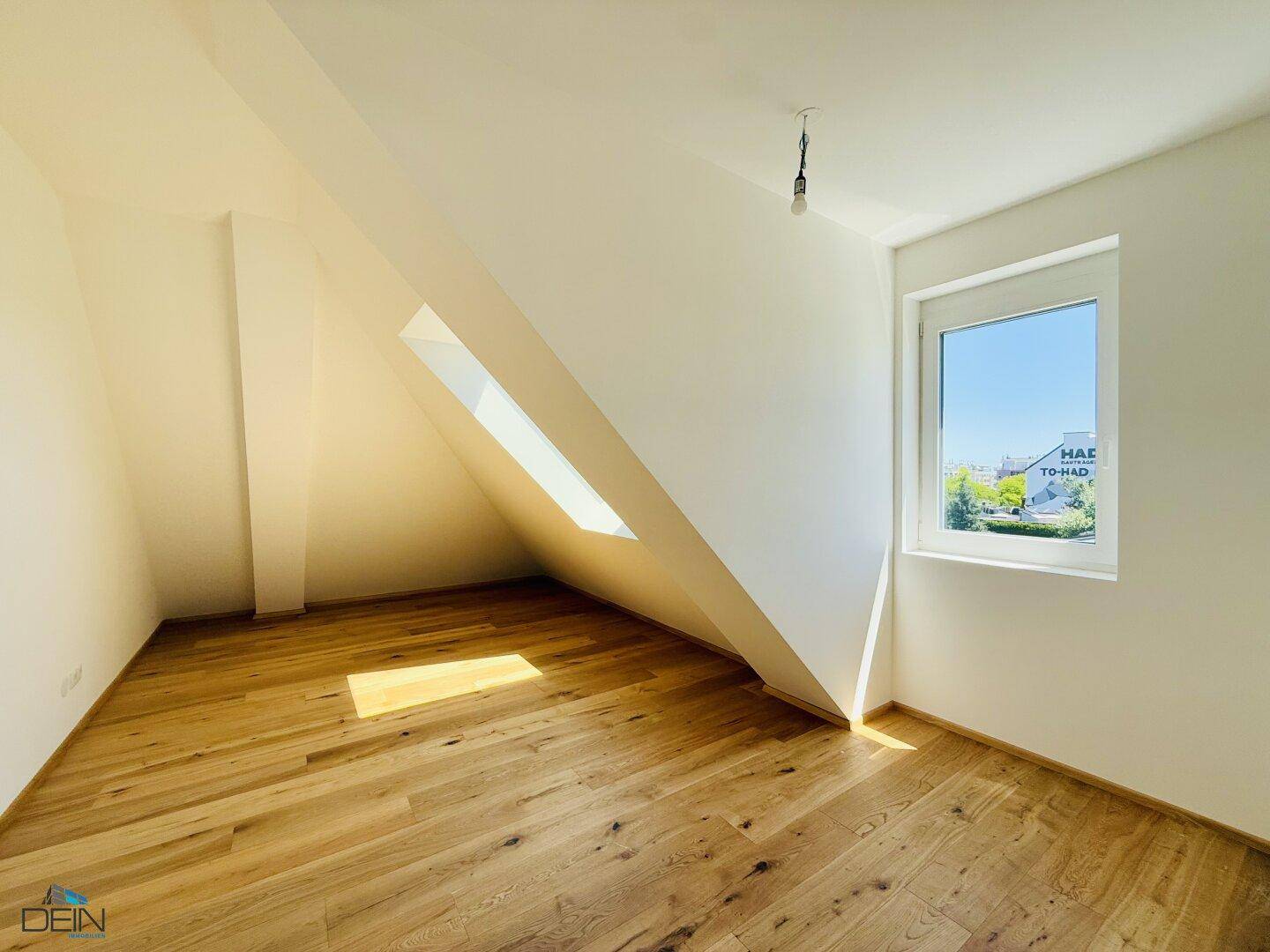 Dachgeschossraum mit Holzboden, schrägen Wänden und einem Fenster mit Weitblick.