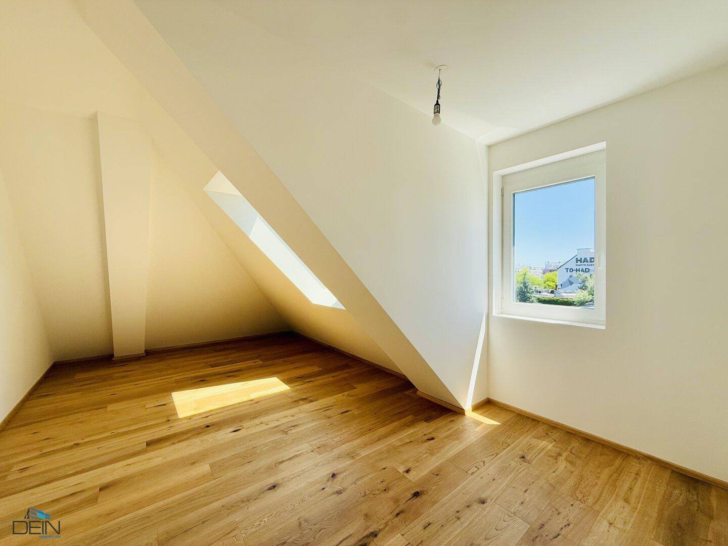 Dachgeschosszimmer mit Holzboden, schrägen Wänden und einem schmalen Dachfenster.