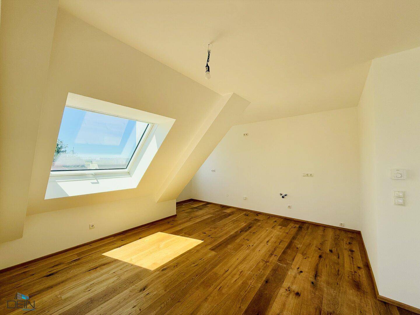 Lichtdurchfluteter Raum im Dachgeschoss mit Holzboden und einem großen Dachfenster.