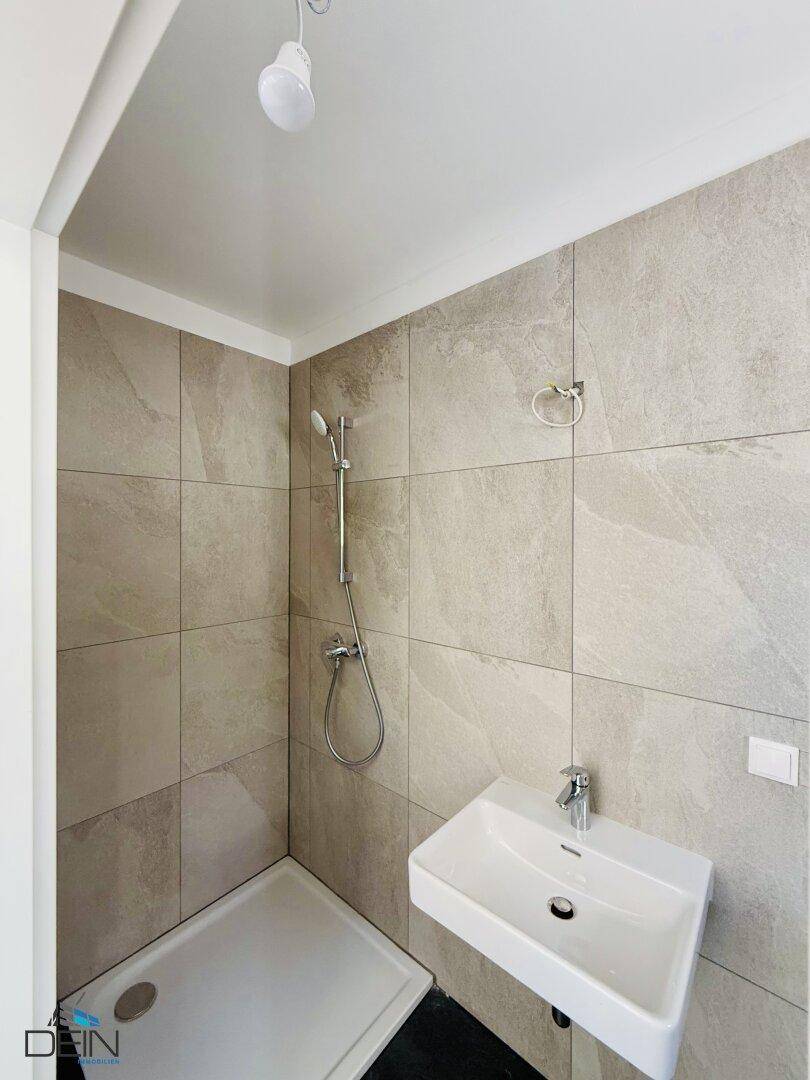 Kleines, modernes Badezimmer mit Duschbereich, Wandwaschbecken und hellgrauen Wandfliesen.