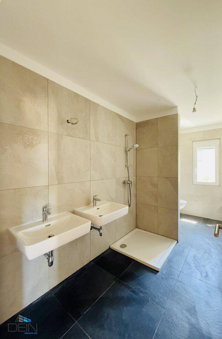 Geräumiges Badezimmer mit zwei Waschbecken, Duschbereich und Fenster für natürliche Belüftung.