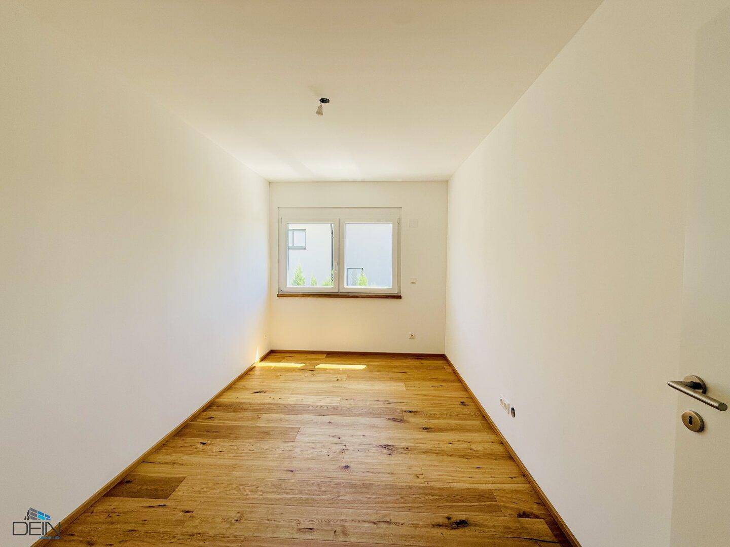 Helles Schlafzimmer mit Eichenparkett und Fenster, das viel Tageslicht hereinlässt.