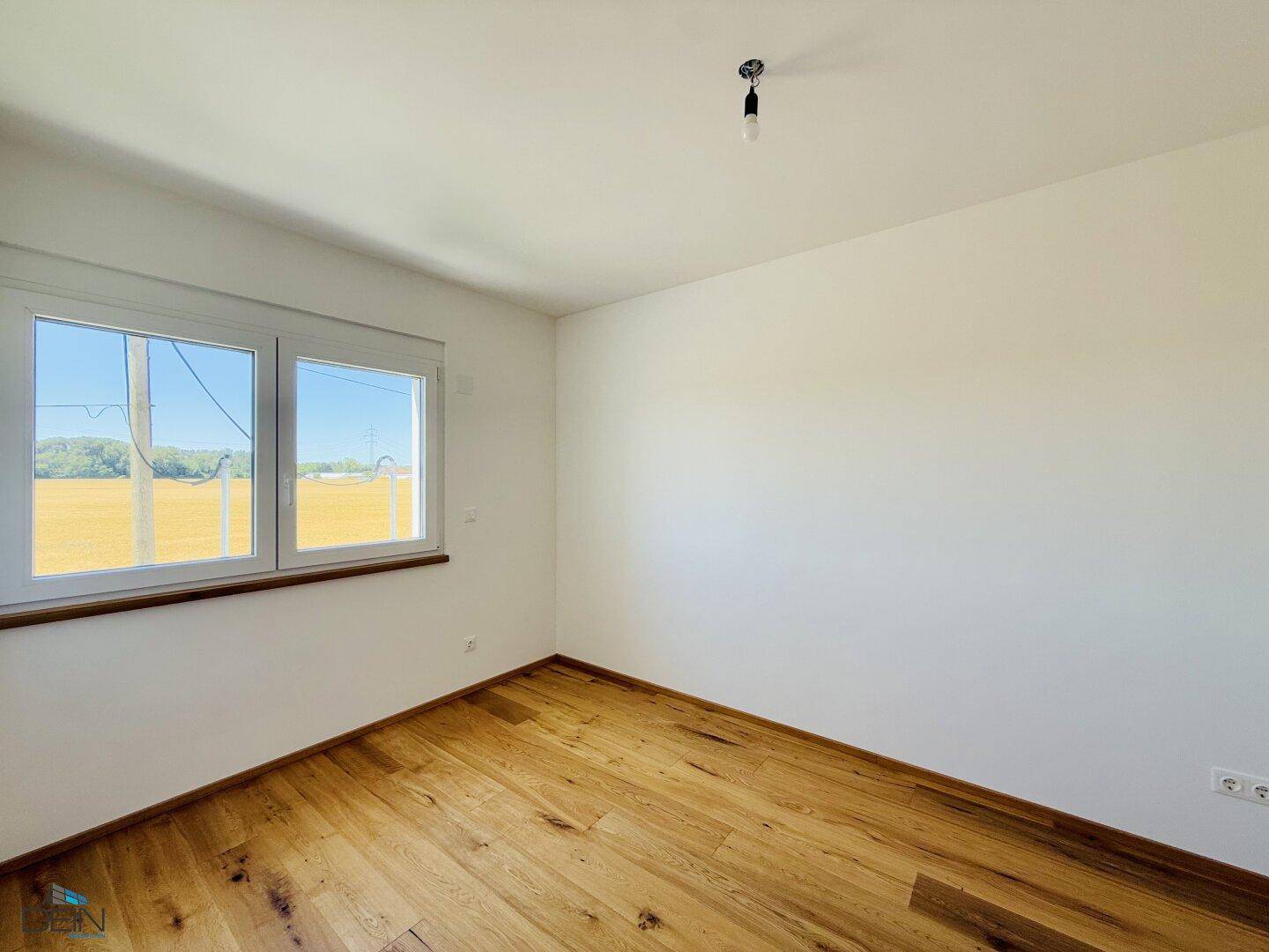 Helles Schlafzimmer mit Eichenparkett und Fenster mit Blick auf die grüne Umgebung.