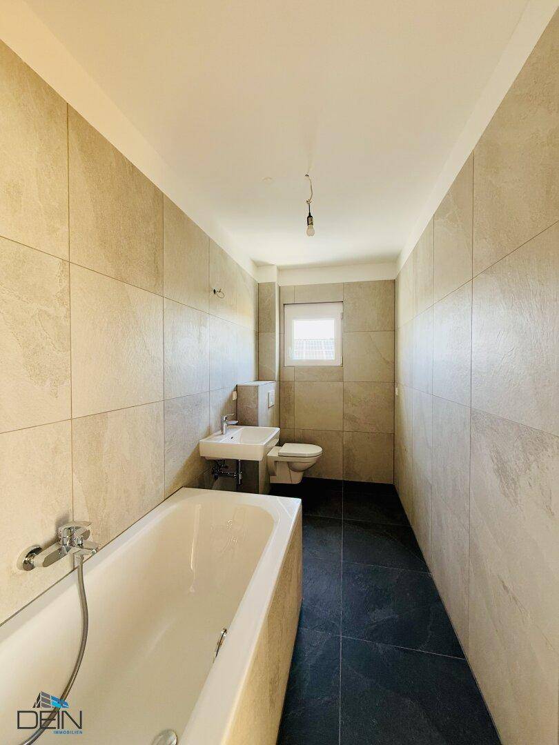 Modernes Badezimmer mit Badewanne, Waschbecken, WC und Fenster für natürliche Belüftung.