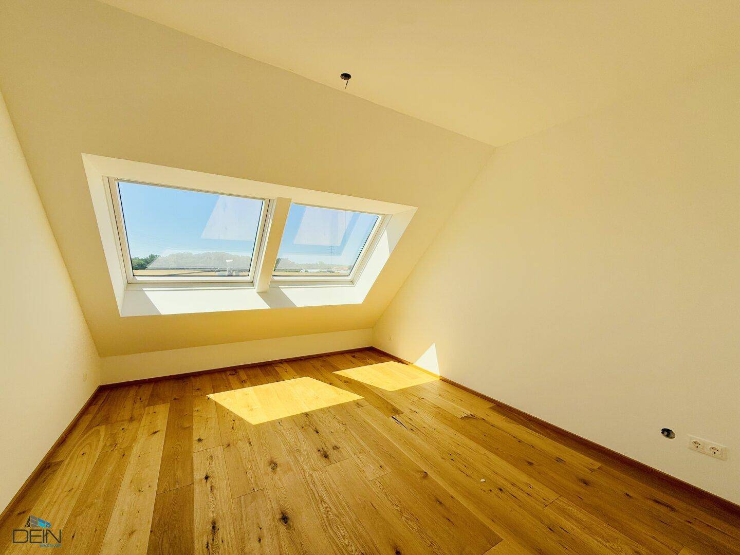 Dachzimmer mit Eichenparkett und großen Dachfenstern, die viel Sonnenlicht hereinlassen.