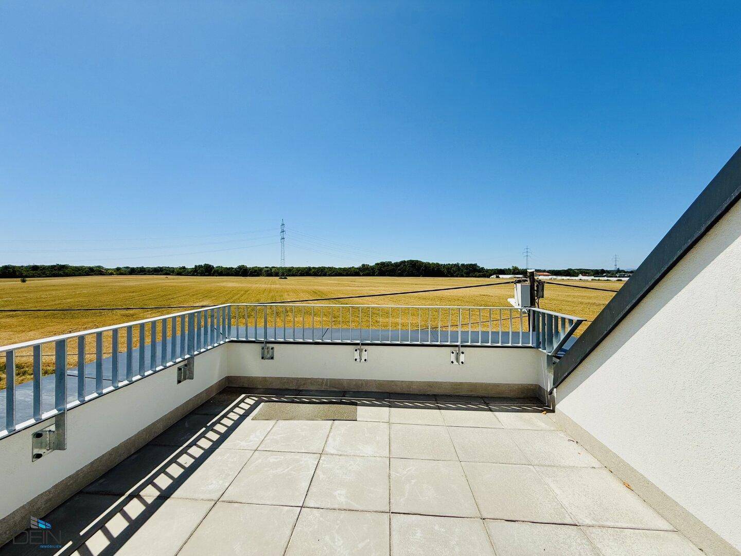 Große Dachterrasse mit weitem Blick über die Felder unter blauem Himmel.