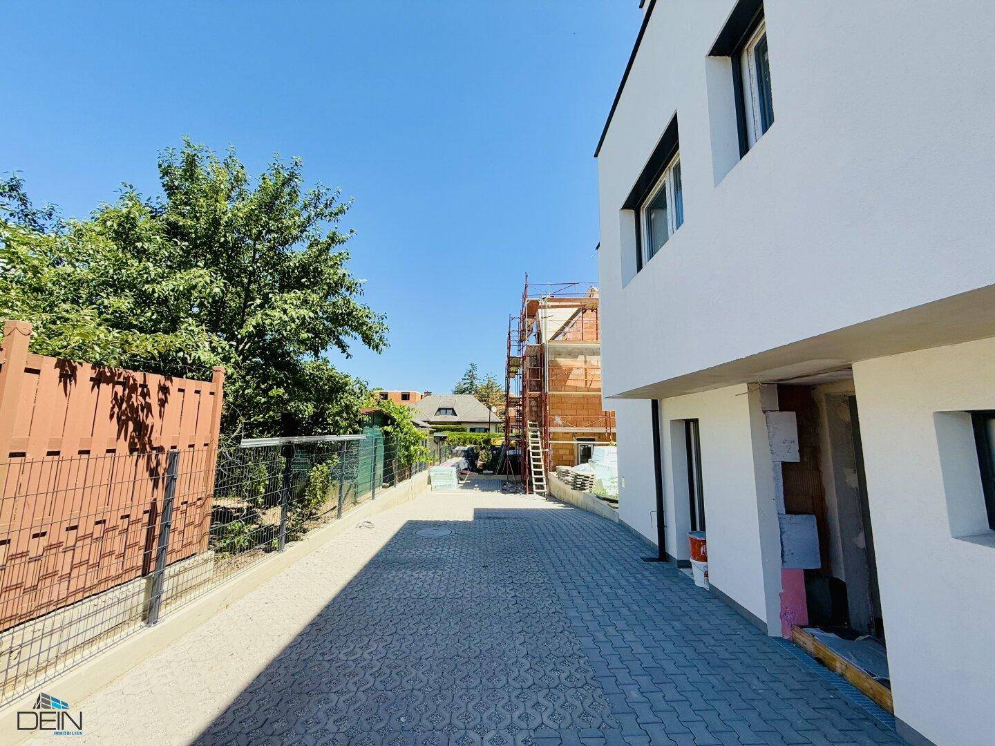 Zufahrt zu den modernen Neubauten mit gepflastertem Weg und angrenzendem Bau.