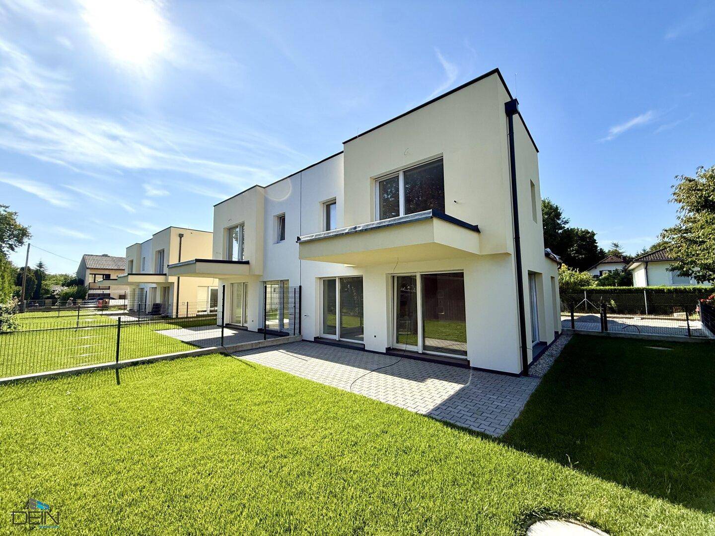 Moderne Doppelhaushälfte mit weißer Fassade, großem Garten und sonniger Terrasse.