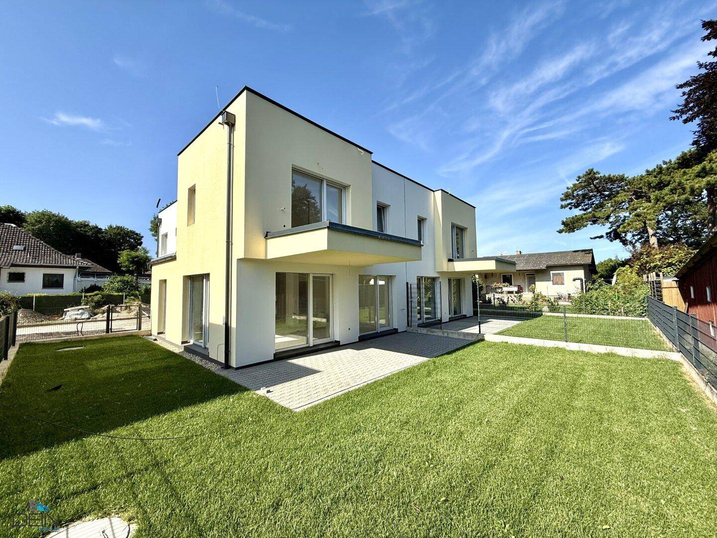 Ansicht einer modernen Neubau-Doppelhaushälfte mit weitläufigem Garten und gepflasterter Terrasse.