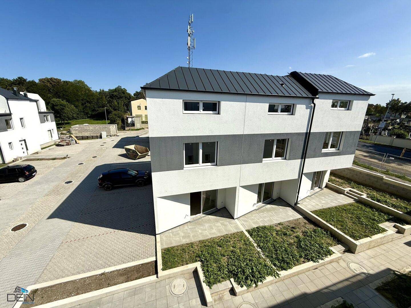 Ansicht der Rückseite eines modernen Reihenhauses mit kleinen Gartenflächen und gepflastertem Zugang.