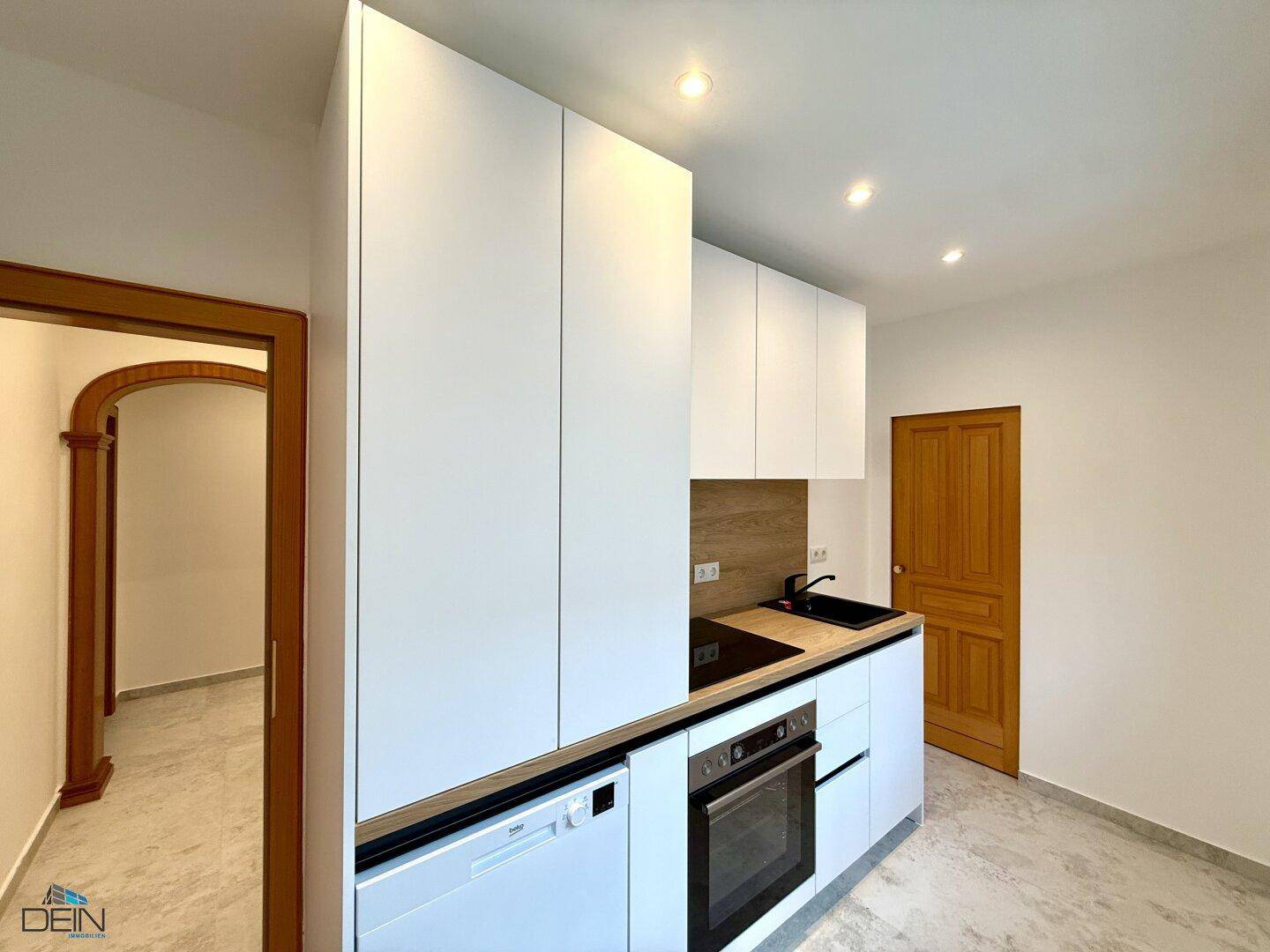 Moderne Einbauküche mit weißen Fronten, integrierten Geräten und Holzdetails.